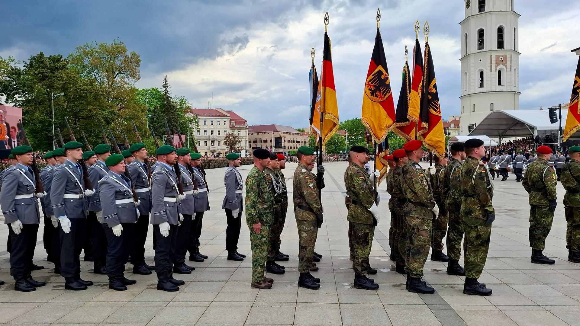 Deutsche Soldaten stehen in Uniformen auf einem öffentlichen Platz in Litauen, einige halten die deutsche Flagge in der Hand. Im Hintergrund ist der Glockenturm der Kathedrale St. Stanislaus in Vilnius zu sehen. Deutsche Soldaten stehen in Uniformen auf einem öffentlichen Platz in Litauen, einige halten die deutsche Flagge in der Hand. Im Hintergrund ist der Glockenturm der Kathedrale St. Stanislaus in Vilnius zu sehen.