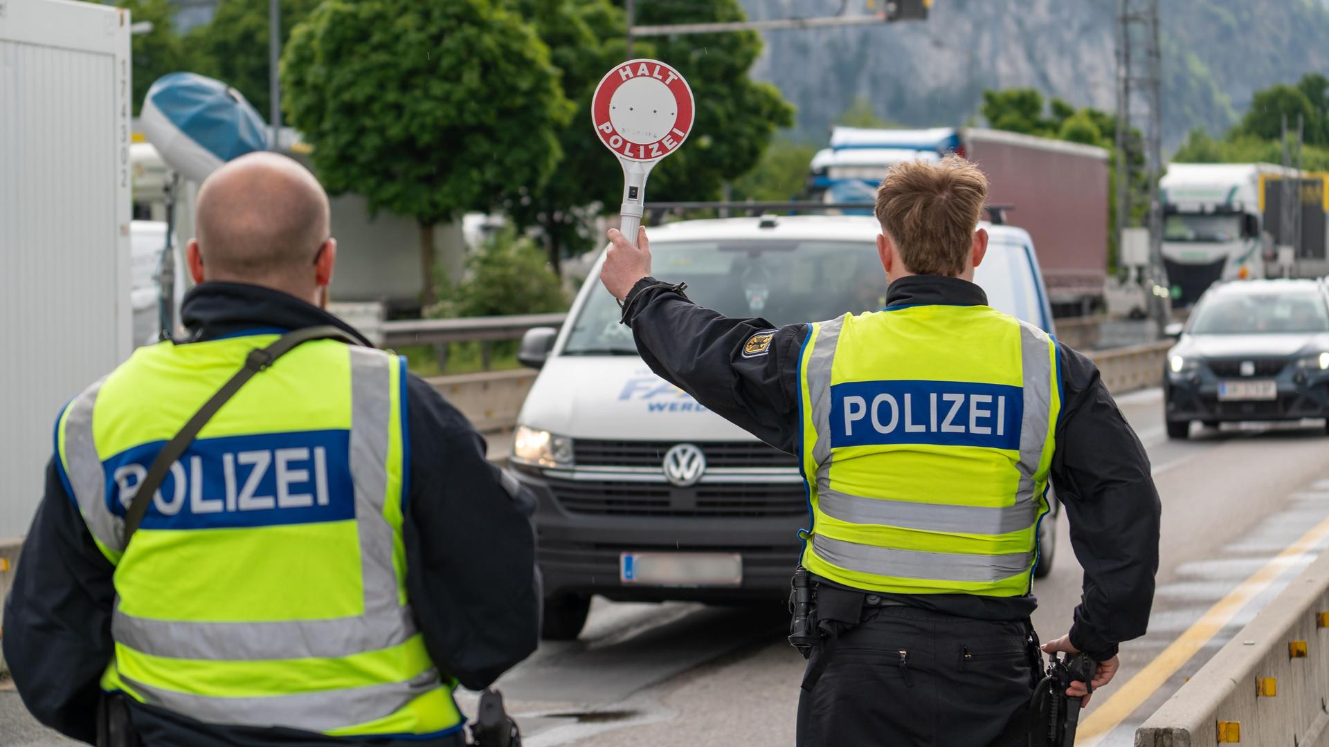 Ein Polizist stoppt an der deutsch-österreichischen Grenze ein Fahrzeug auf der Autobahn mit einer Polizeikelle mit Aufschrift: HALT POLIZEI. Ein Polizist stoppt an der deutsch-österreichischen Grenze ein Fahrzeug auf der Autobahn mit einer Polizeikelle mit Aufschrift: HALT POLIZEI.