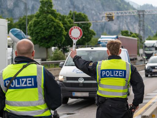 Ein Polizist stoppt an der deutsch-österreichischen Grenze ein Fahrzeug auf der Autobahn mit einer Polizeikelle mit Aufschrift: HALT POLIZEI.