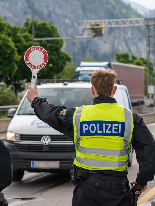 Ein Polizist stoppt an der deutsch-österreichischen Grenze ein Fahrzeug auf der Autobahn mit einer Polizeikelle mit Aufschrift: HALT POLIZEI.
