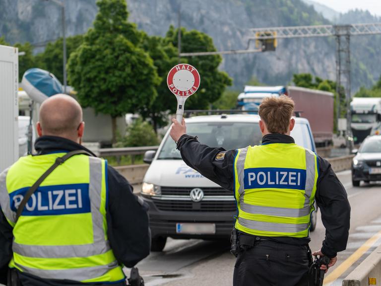 Ein Polizist stoppt an der deutsch-österreichischen Grenze ein Fahrzeug auf der Autobahn mit einer Polizeikelle mit Aufschrift: HALT POLIZEI.