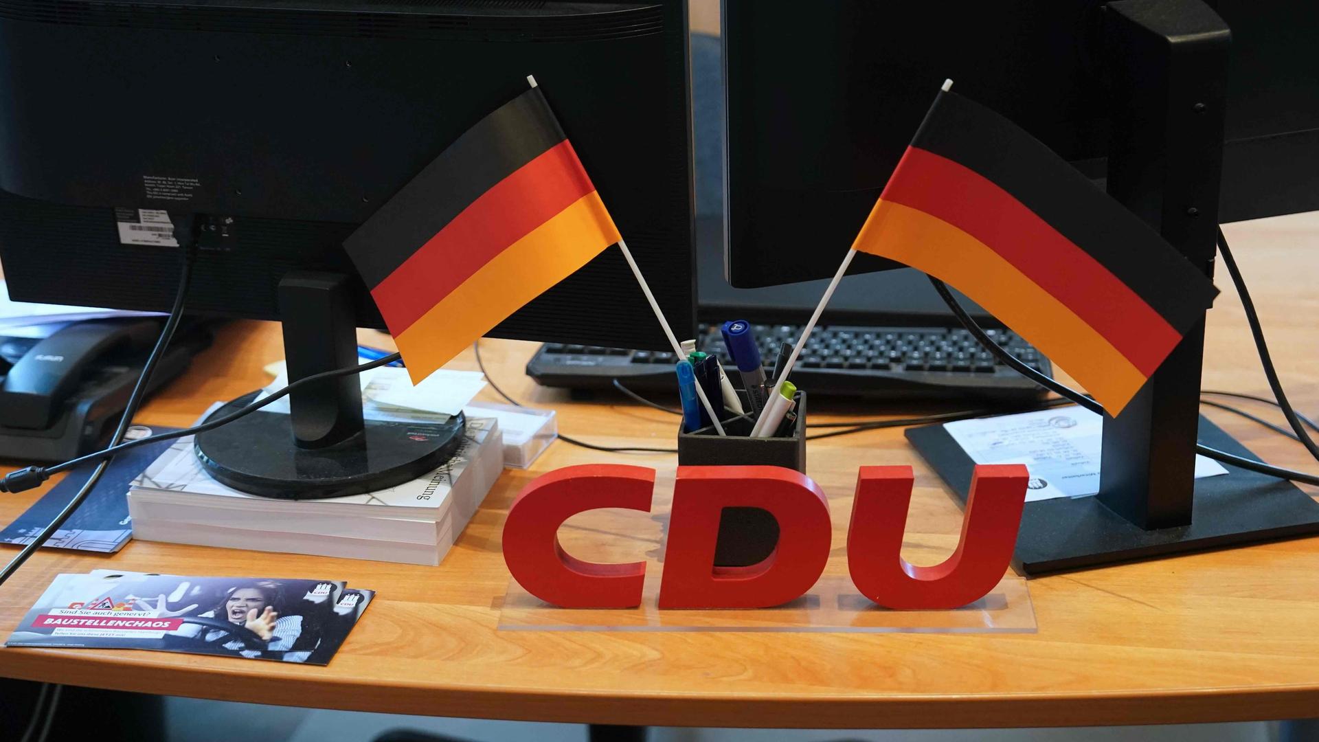 Ein CDU-Logo und zwei Deutschlandflaggen stehen auf einem Schreibtisch in der CDU-Landesgeschäftsstelle.