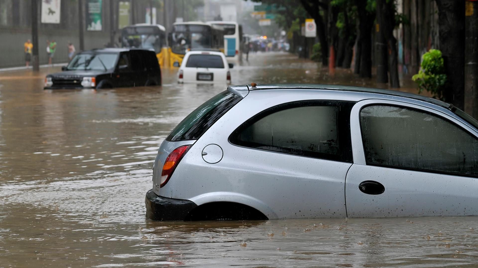 Ein Auto steckt nach einem Starkregen in der Stadt in den Fluten fest, das Wasser steht bis zum Autofenster.