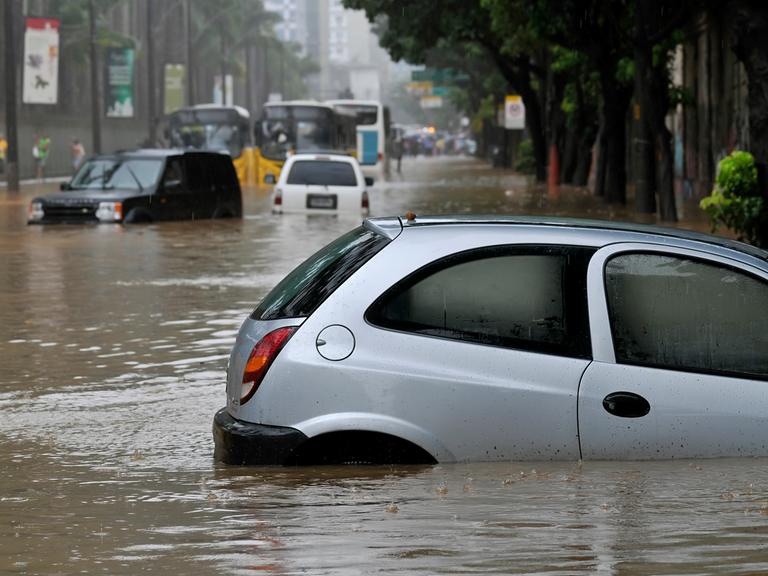 Ein Auto steckt nach einem Starkregen in der Stadt in den Fluten fest, das Wasser steht bis zum Autofenster.