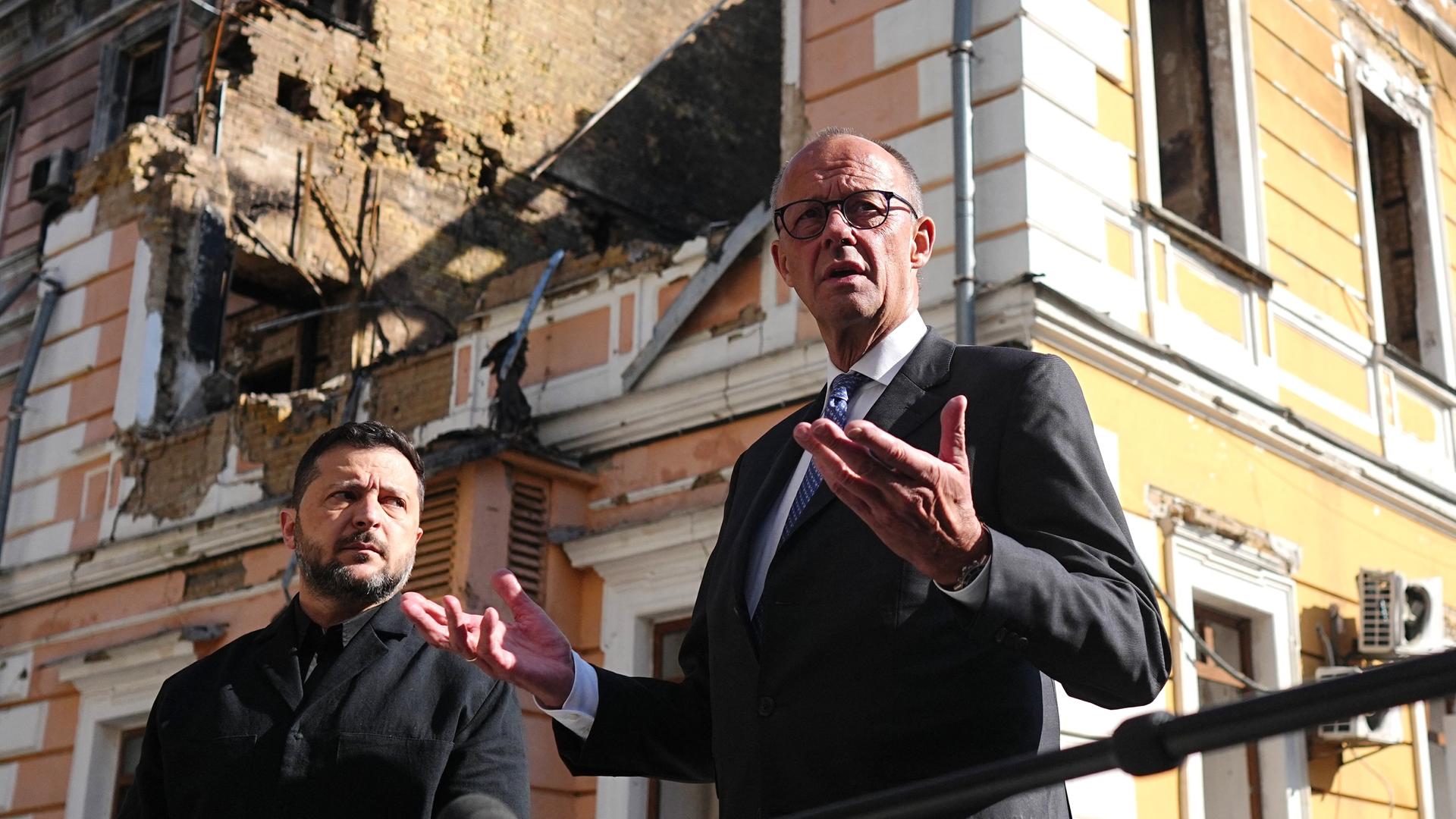 Bundeskanzler Friedrich Merz (r, CDU) und Wolodymyr Selenskyj (l), Präsident der Ukraine, stehen am zerstörten Gebäude der Nationalen Akademie der Wissenschaften. Aufnahmedatum: 4. Oktober 2026.