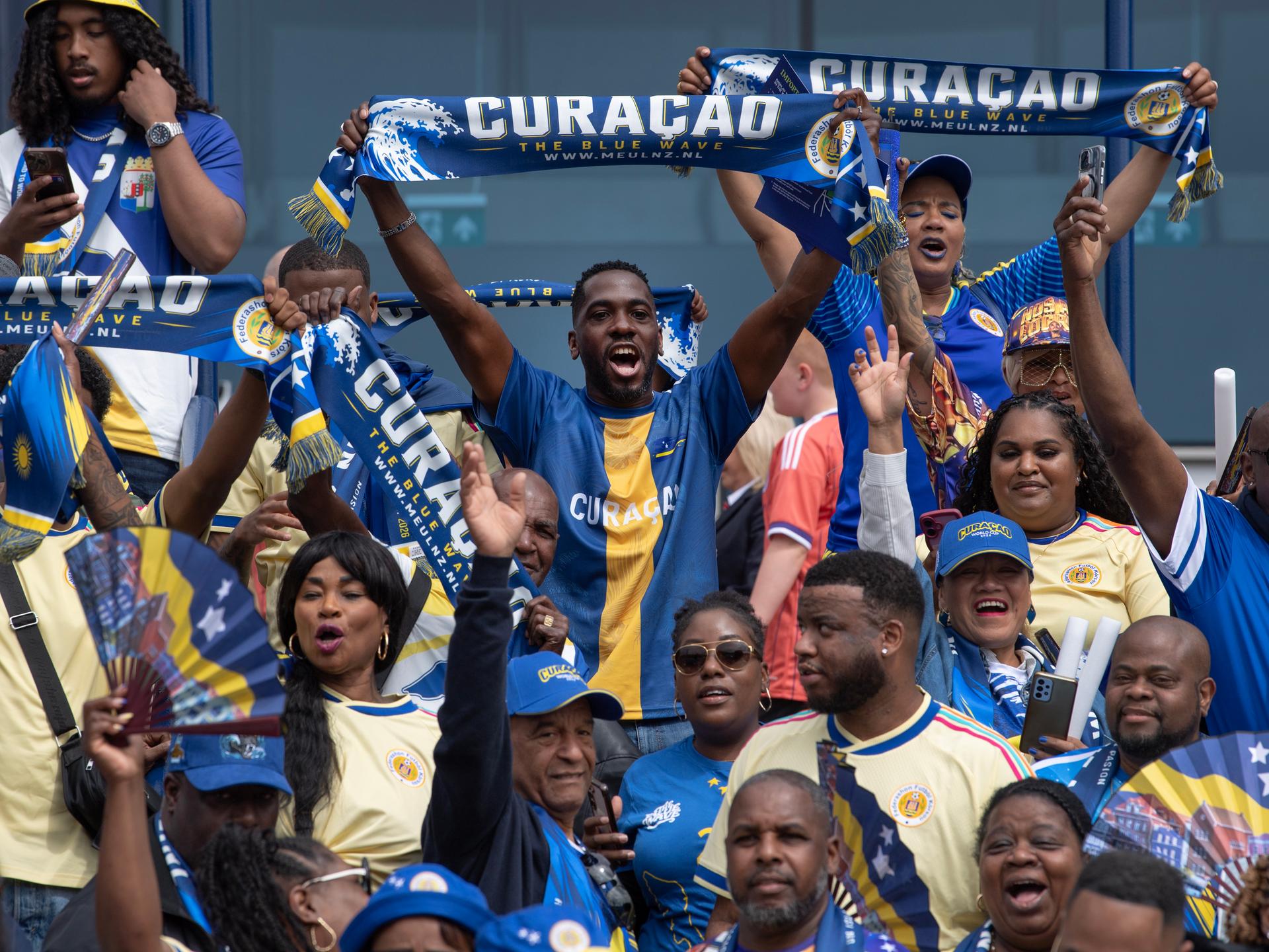 Fans aus Curaçao bei einem Länderspiel zwischen Schottland und Curaçao im Mai 2026. Die Fans feiern fröhlich und halten blaue Curaçaoschals und Fächer.