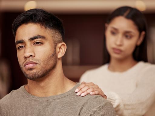 Ein Mann steht vor einer Frau, sie berührt ihn an der Schulter.