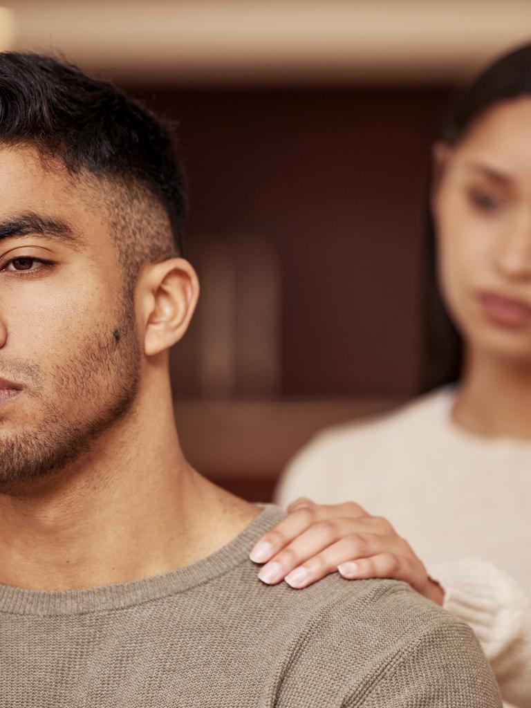 Ein Mann steht vor einer Frau, sie berührt ihn an der Schulter.