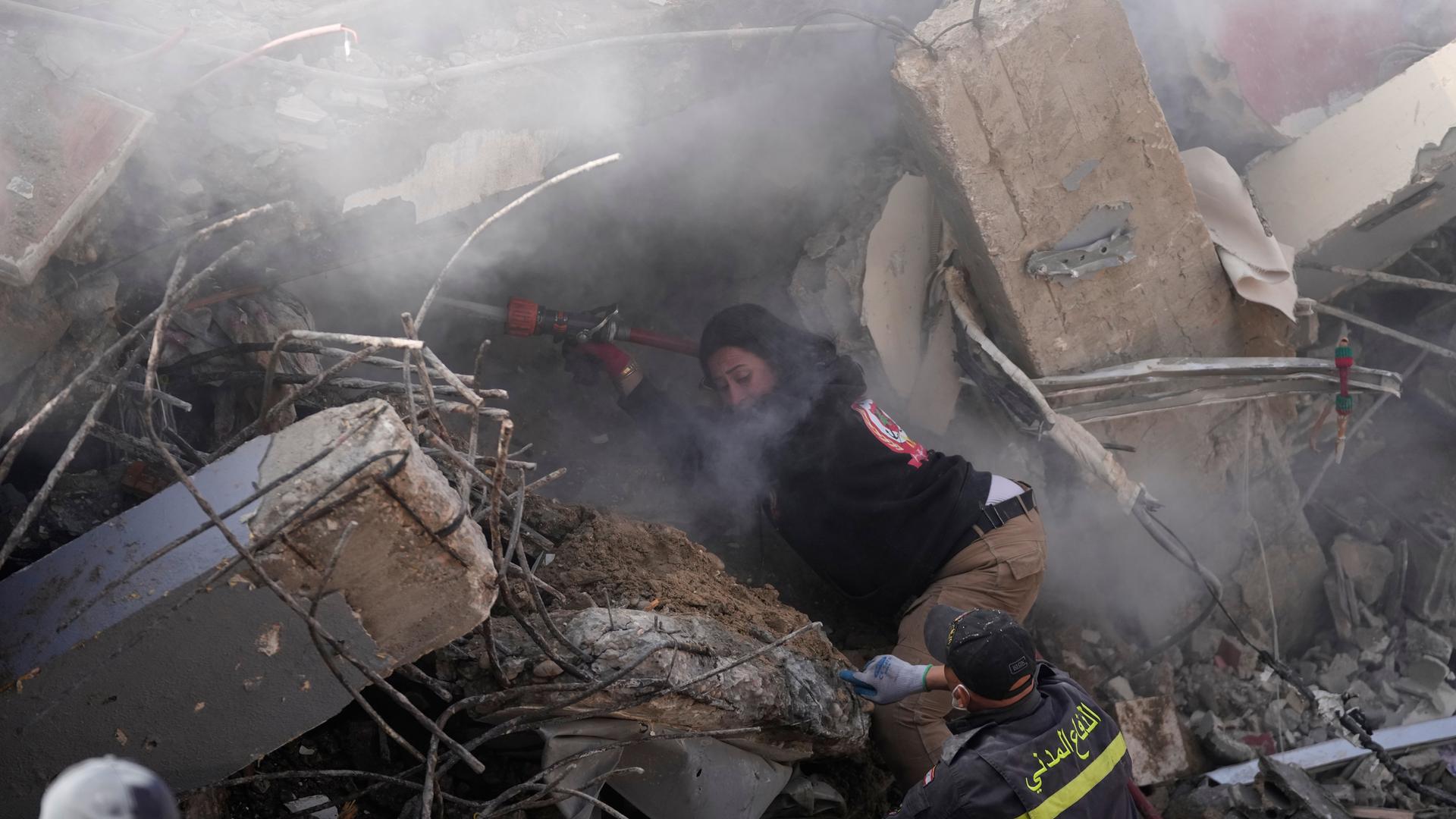 Eine Feuerwehrfrau sprüht Wasser, um den Staub zu reduzieren, während Rettungskräfte in einem zerstörten Gebäude, das im Südlibanon von einem israelischen Luftangriff getroffen wurde, nach Opfern suchen. 