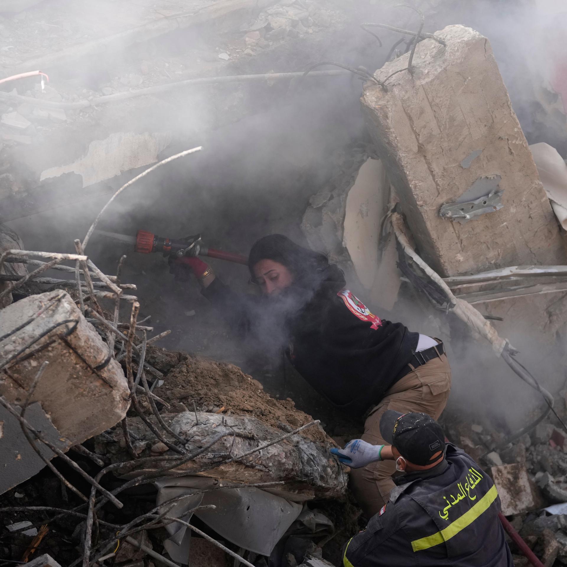 Eine Feuerwehrfrau sprüht Wasser, um den Staub zu reduzieren, während Rettungskräfte in einem zerstörten Gebäude, das im Südlibanon von einem israelischen Luftangriff getroffen wurde, nach Opfern suchen. 