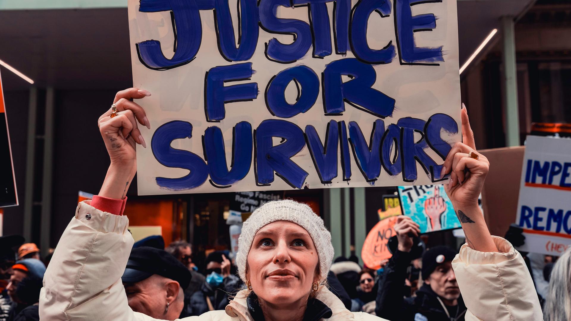 Auf einer Demonstration vor dem Trump Tower hält eine Frau ein Schild mit der Aufschrift "Gerechtigkeit für die Überlebenden" hoch.