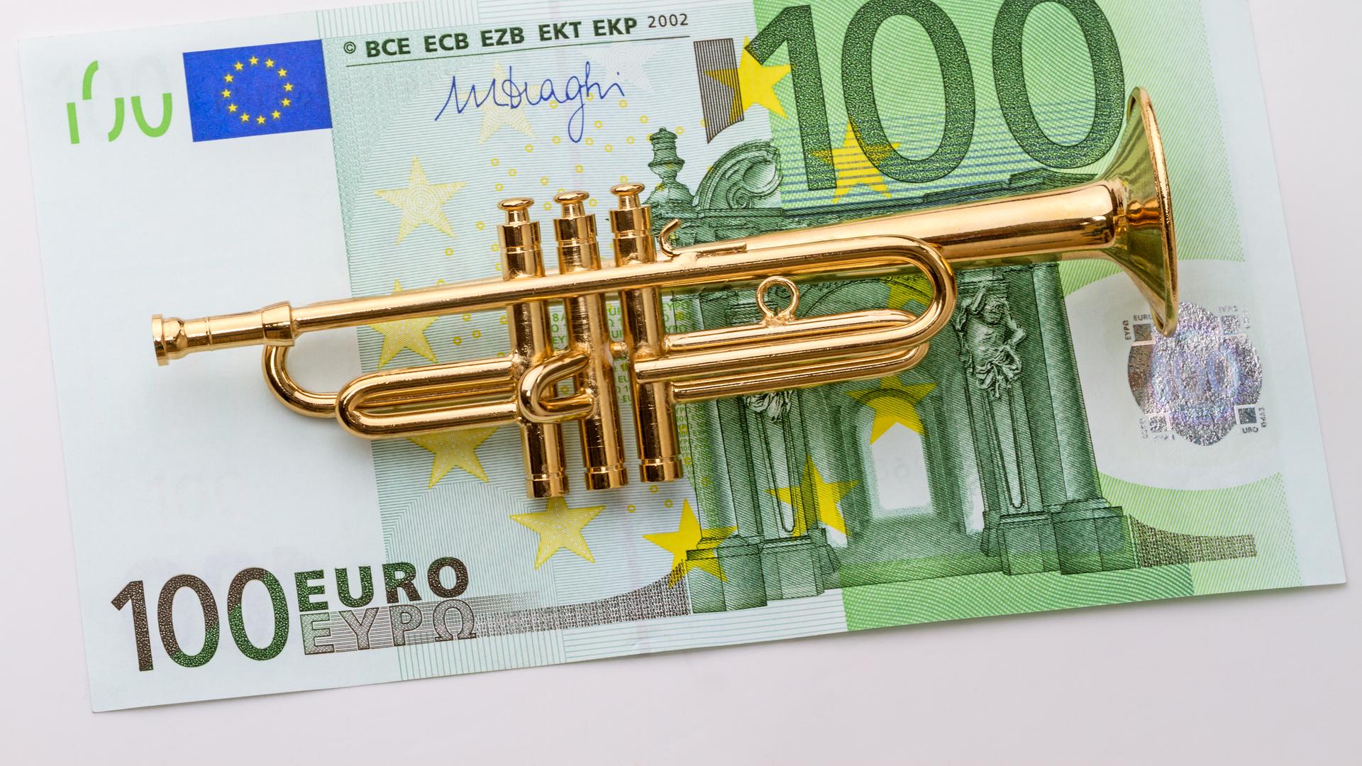 Eine kleine Modelltrompete liegt auf einem 100-Euro-Schein. Eine kleine Modelltrompete liegt auf einem 100-Euro-Schein.
