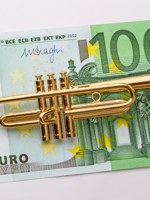 Eine kleine Modelltrompete liegt auf einem 100-Euro-Schein.