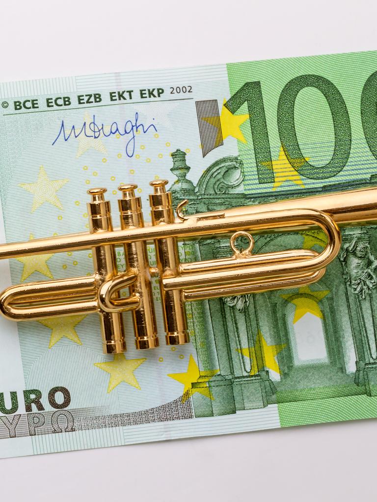 Eine kleine Modelltrompete liegt auf einem 100-Euro-Schein.