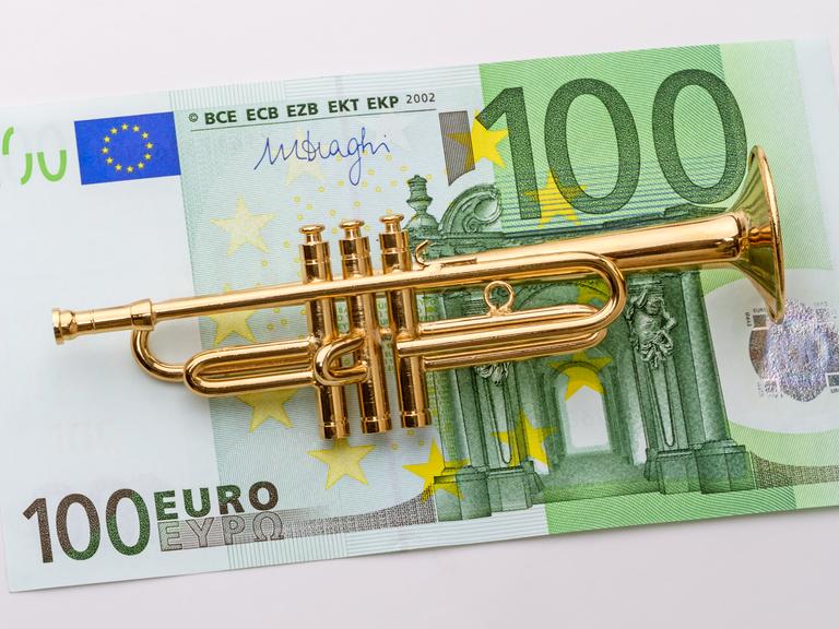 Eine kleine Modelltrompete liegt auf einem 100-Euro-Schein.