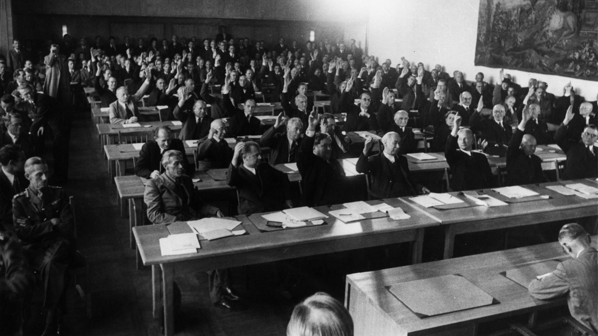 Annahme des Grundgesetzes: Das Plenum des Parlamentarischen Rates nimmt in 3. Lesung am 8. Mai 1949 den revidierten Grundgesetzentwurf mit 53 gegen 12 Stimmen an.