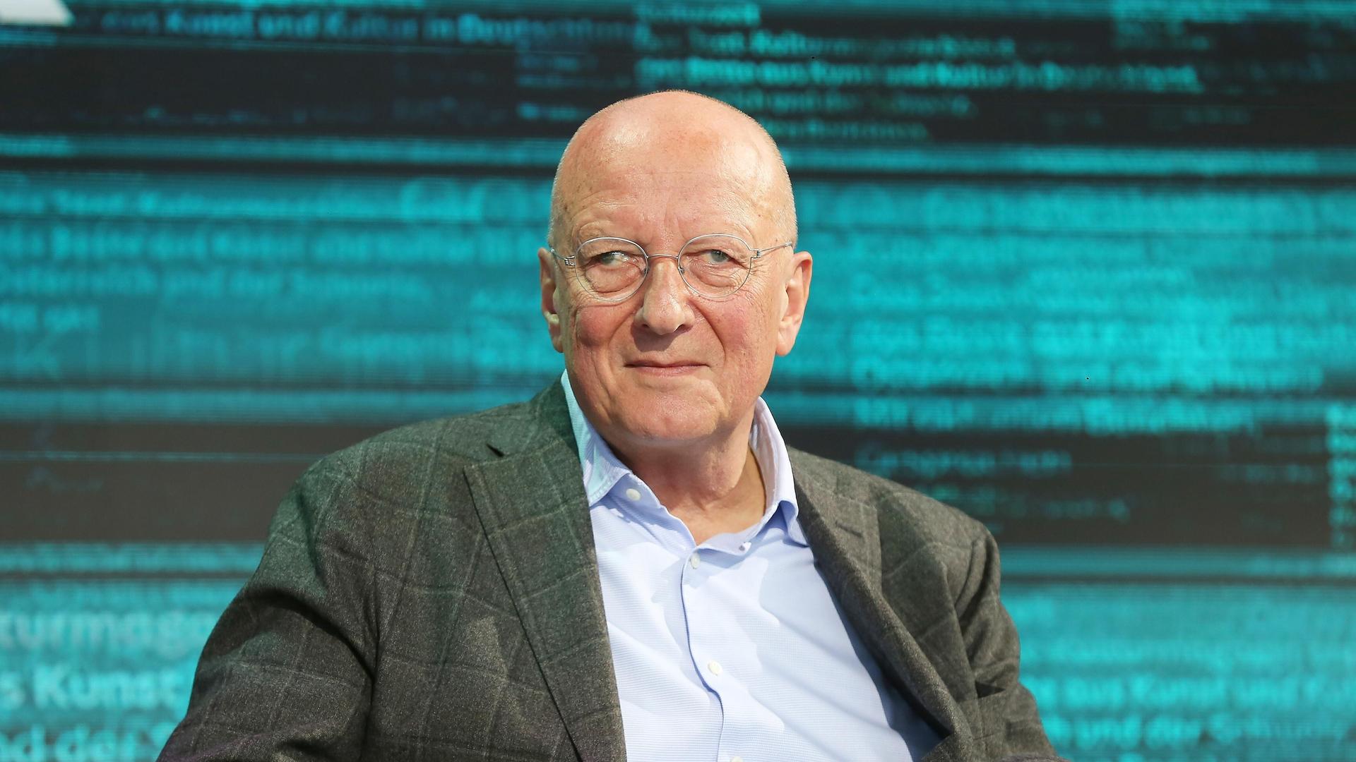 Der Schweizer Publizist Roger de Weck trägt ein hellblaues Hemd und ein kariertes Sakko. Er sitzt während der Leipziger Buchmesse auf einer bühne und schaut in die Kamera.