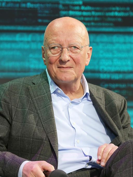 Der Schweizer Publizist Roger de Weck trägt ein hellblaues Hemd und ein kariertes Sakko. Er sitzt während der Leipziger Buchmesse auf einer bühne und schaut in die Kamera.