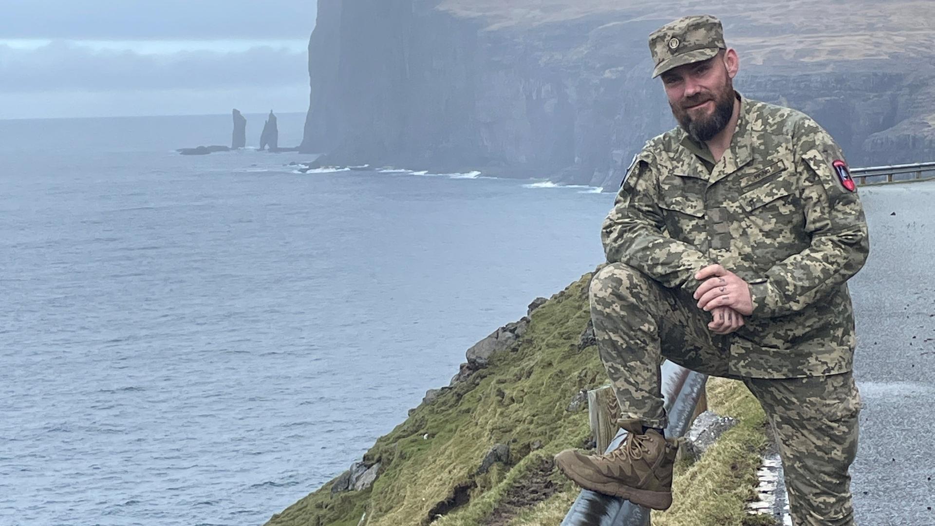 Bjørn Kallsoys steht an einer Klippe in seiner Uniform im rechten Bildrand und lächelt in die Kamera.