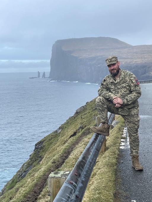 Bjørn Kallsoys steht an einer Klippe in seiner Uniform im rechten Bildrand und lächelt in die Kamera.