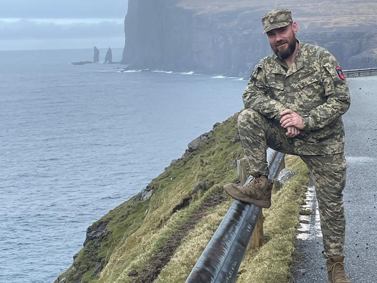 Bjørn Kallsoys steht an einer Klippe in seiner Uniform im rechten Bildrand und lächelt in die Kamera.