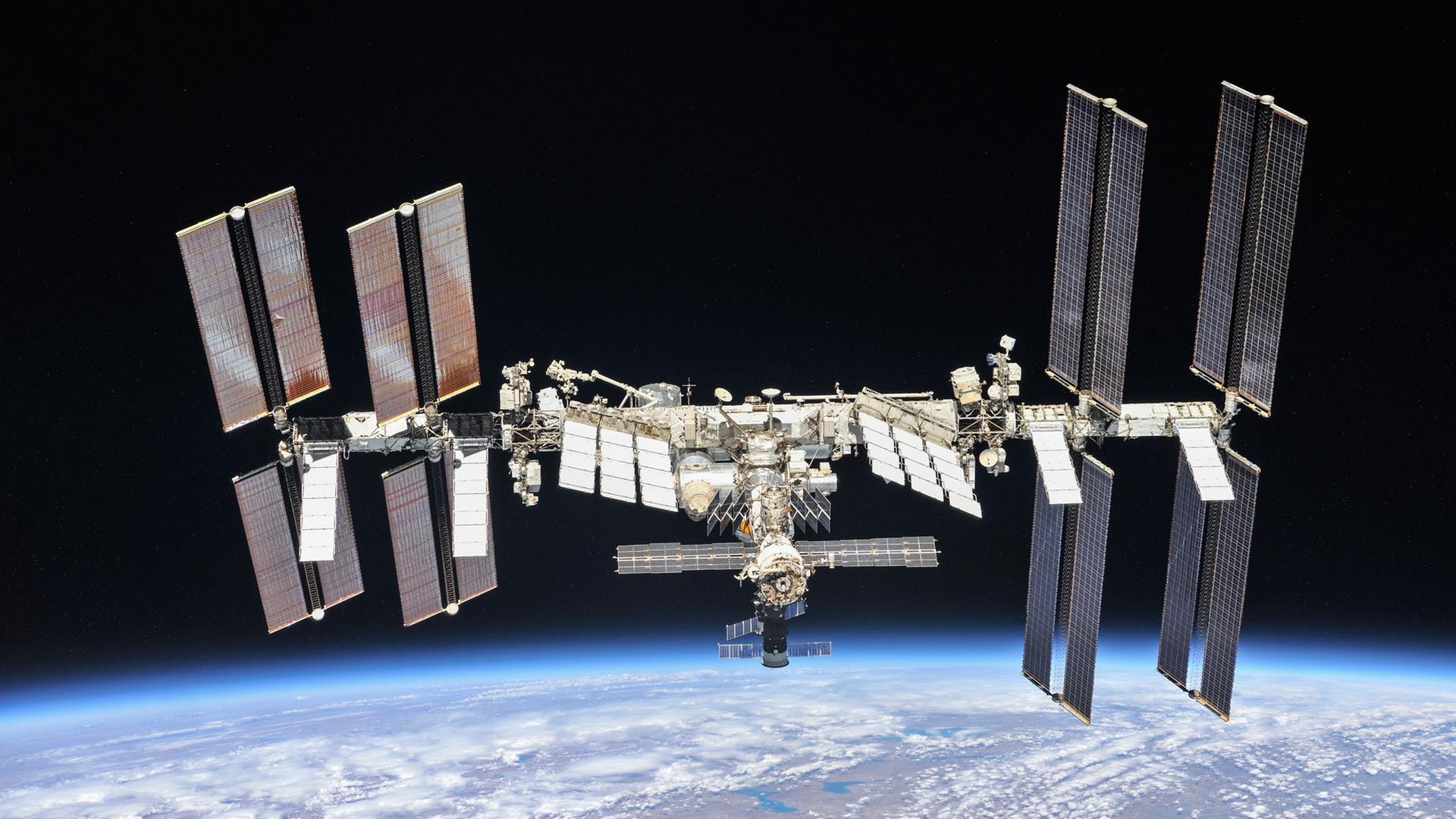 Die Internationale Raumstation in der Schwärzes des Alls, am unteren Bildrand der blaue Planet Erde