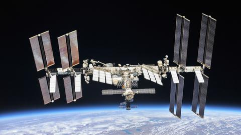 Die Internationale Raumstation in der Schwärzes des Alls, am unteren Bildrand der blaue Planet Erde