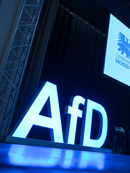 AfD-Schriftzug und das AfD-Logo auf der Bühne einem Versammlungssaal. AfD-Schriftzug und das AfD-Logo auf der Bühne einem Versammlungssaal.