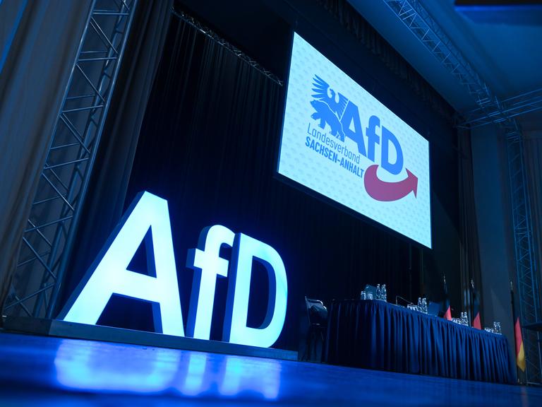 AfD-Schriftzug und das AfD-Logo auf der Bühne einem Versammlungssaal. AfD-Schriftzug und das AfD-Logo auf der Bühne einem Versammlungssaal.