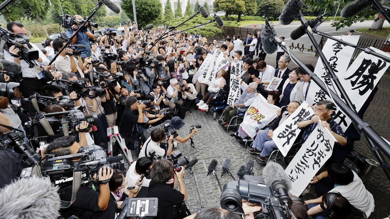 Die Kläger, ihre Anwälte und Unterstützer halten vor dem Obersten Gerichtshof Schilder mit der Aufschrift "Gewonnener Prozess" in Tokio, Japan. 