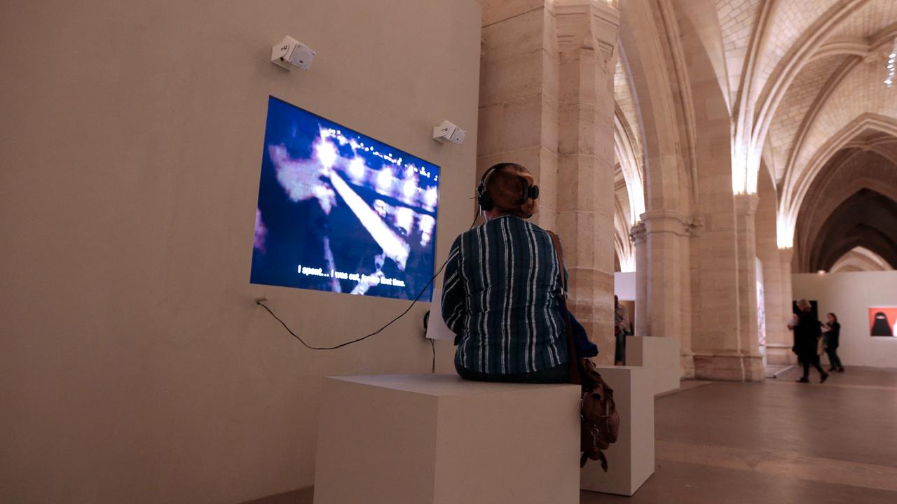 Eine Besucherin betrachtet einen Videobildschirm an einer Wand im Louvre und hat Kopfhörer auf