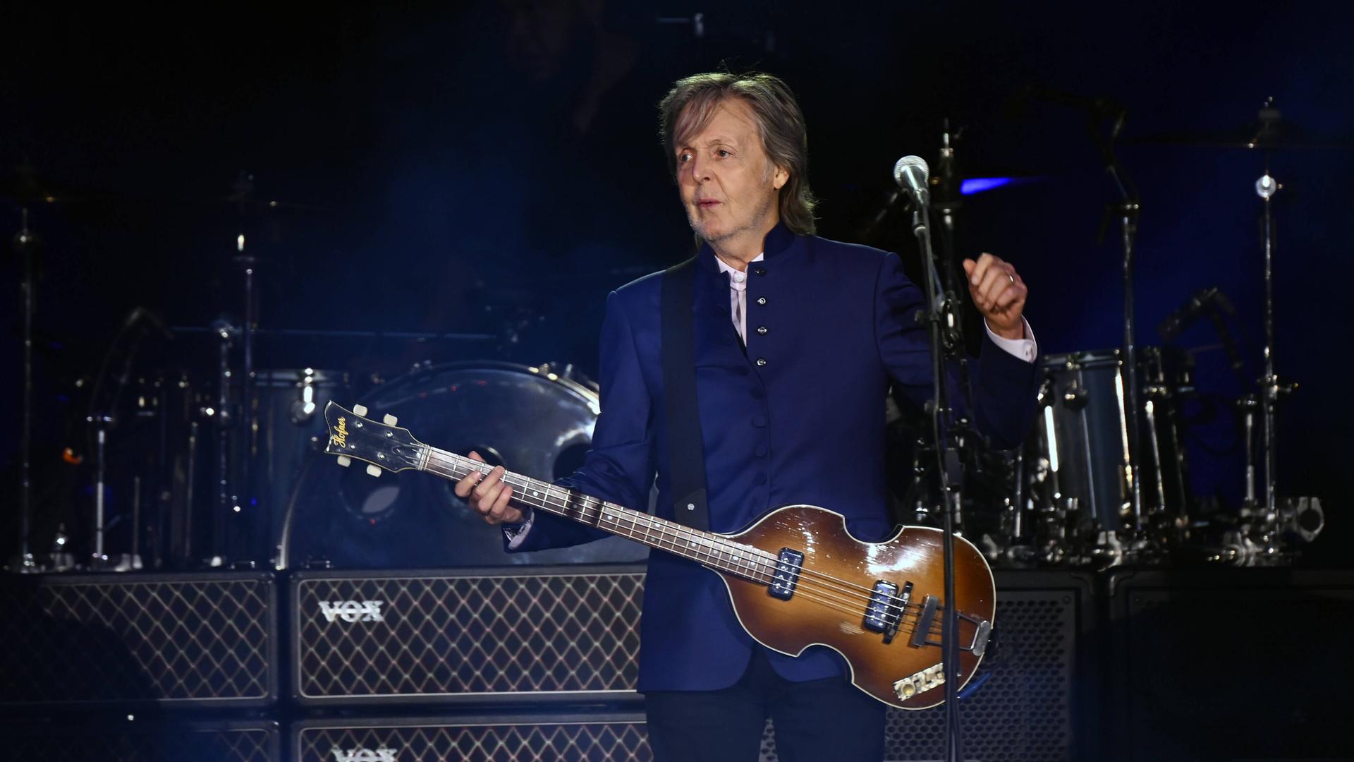 Ein Mann mit Gitarre steht auf einer Bühne. Er trägt eine dunkelblaue Jacke. Es ist der frühere Beatle Paul McCartney.