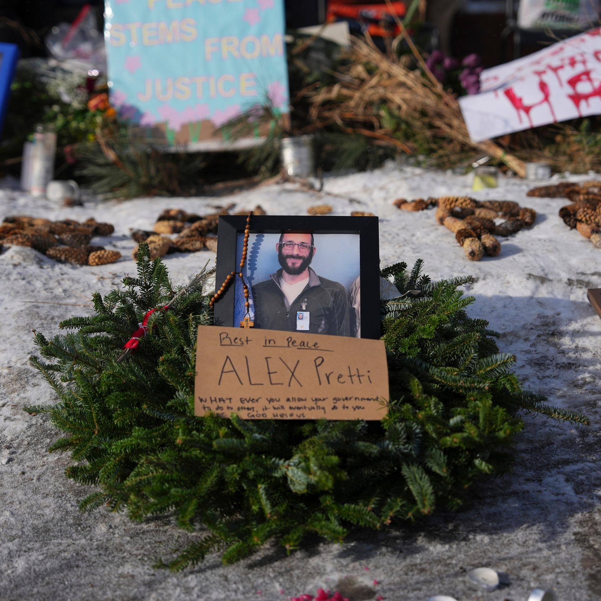 Ein Tannenkranz mit einem Foto Prettis liegt in der Bildmitte auf Schnee. Dahinter weitere Kränze, Schilder und noch ein Bild Prettis. 