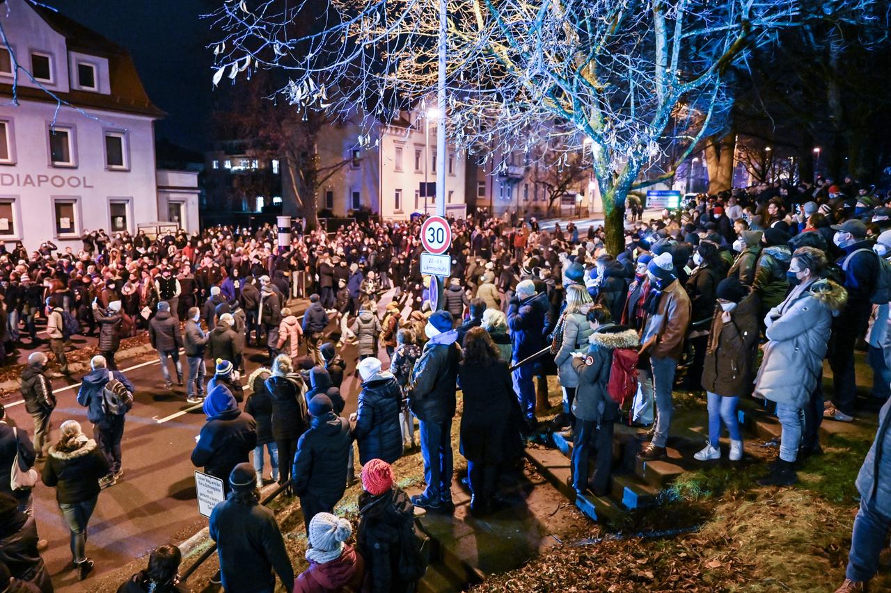 Passanten schauen den Teilnehmern eines sogenannten Spazierganges gegen die Corona-Maßnahmen durch die Innenstadt von Ravensburg zu.  