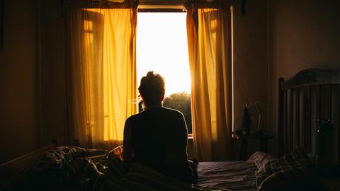 Theresas Zusammenbruch ist spätes Aufbegehren. Sie ist nicht krank, sie will raus. Zu sehen, Eine Frau, mit dem Rücken zur Kamera, sitzt auf einem Bett und schaut zum Fenster hinaus. 