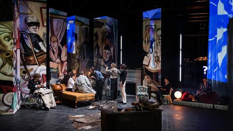 Eine Szene aus der Inszenierung "Der große Kunstraub" mit etlichen Bildteilen im Hintergrund mehrerer Akteure.