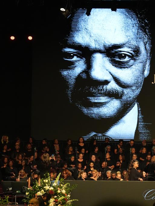Menschen versammeln sich im Haus der Hoffnung. Im Hintergrund zu sehen ist ein Bild des verstorbenen US-Bürgerrechtlers Jesse Jackson.