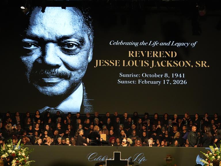 Menschen versammeln sich im Haus der Hoffnung. Im Hintergrund zu sehen ist ein Bild des verstorbenen US-Bürgerrechtlers Jesse Jackson.