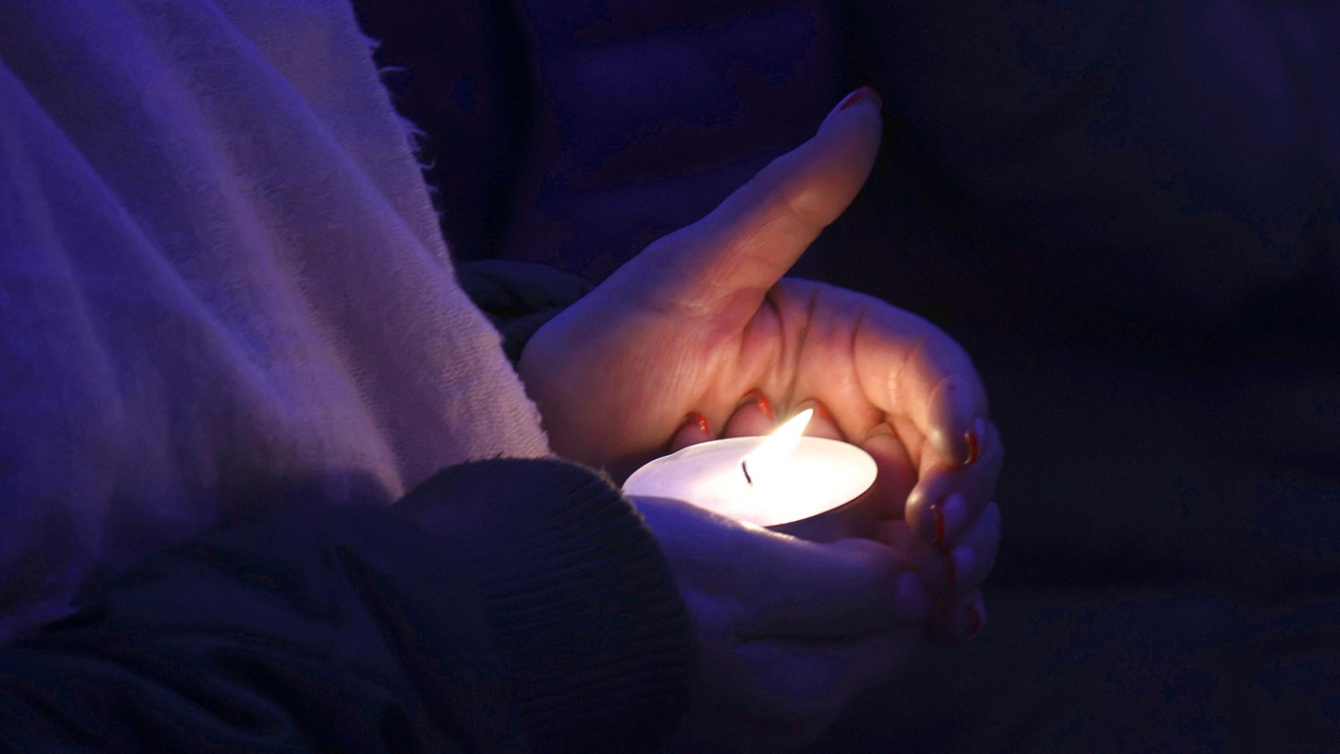 Zwei Hände halten ein brennendes Teelicht bei einer Gedenkfeier für die ukrainischen Opfer eines russischen Luftschlags auf das Mariupol Theater 2022