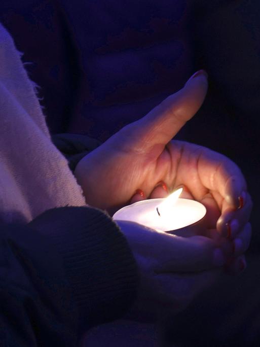 Zwei Hände halten ein brennendes Teelicht bei einer Gedenkfeier für die ukrainischen Opfer eines russischen Luftschlags auf das Mariupol Theater 2022