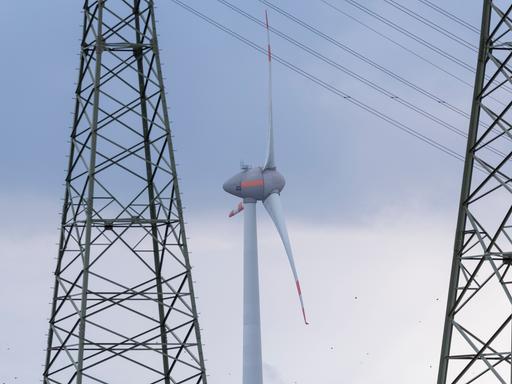 Ein Windrad dreht sich zwischen zwei Strommasten. Ein Windrad dreht sich zwischen zwei Strommasten.