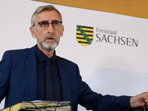 Armin Schuster (CDU), Innenminister in Sachsen, nimmt vor der Pressekonferenz zur Sitzung des sächsischen Kabinetts in der Offizierschule des Heeres im Scharnhorst-Saal auf dem Podium Platz und hält dabei eine Aktenmappe und eine Tasche in den Händen.
