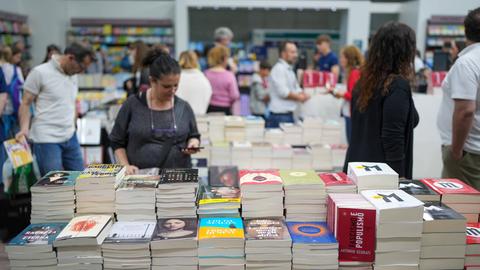 Besucher streifen um Stände mit Bücherstapeln herum.