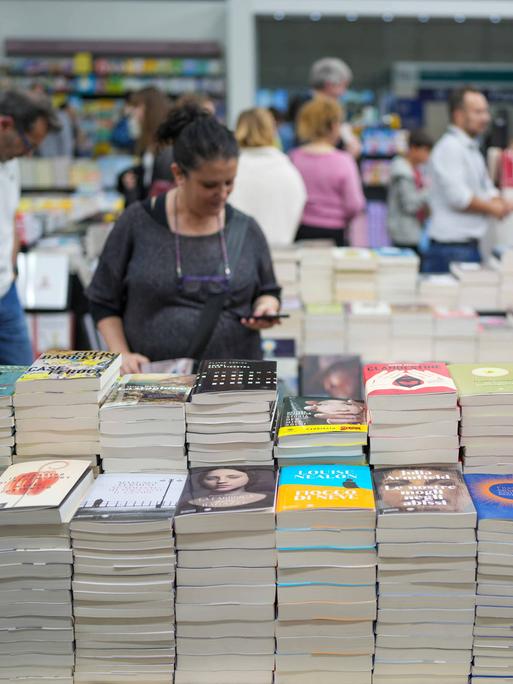 Besucher streifen um Stände mit Bücherstapeln herum.