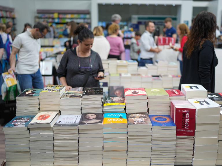 Besucher streifen um Stände mit Bücherstapeln herum.