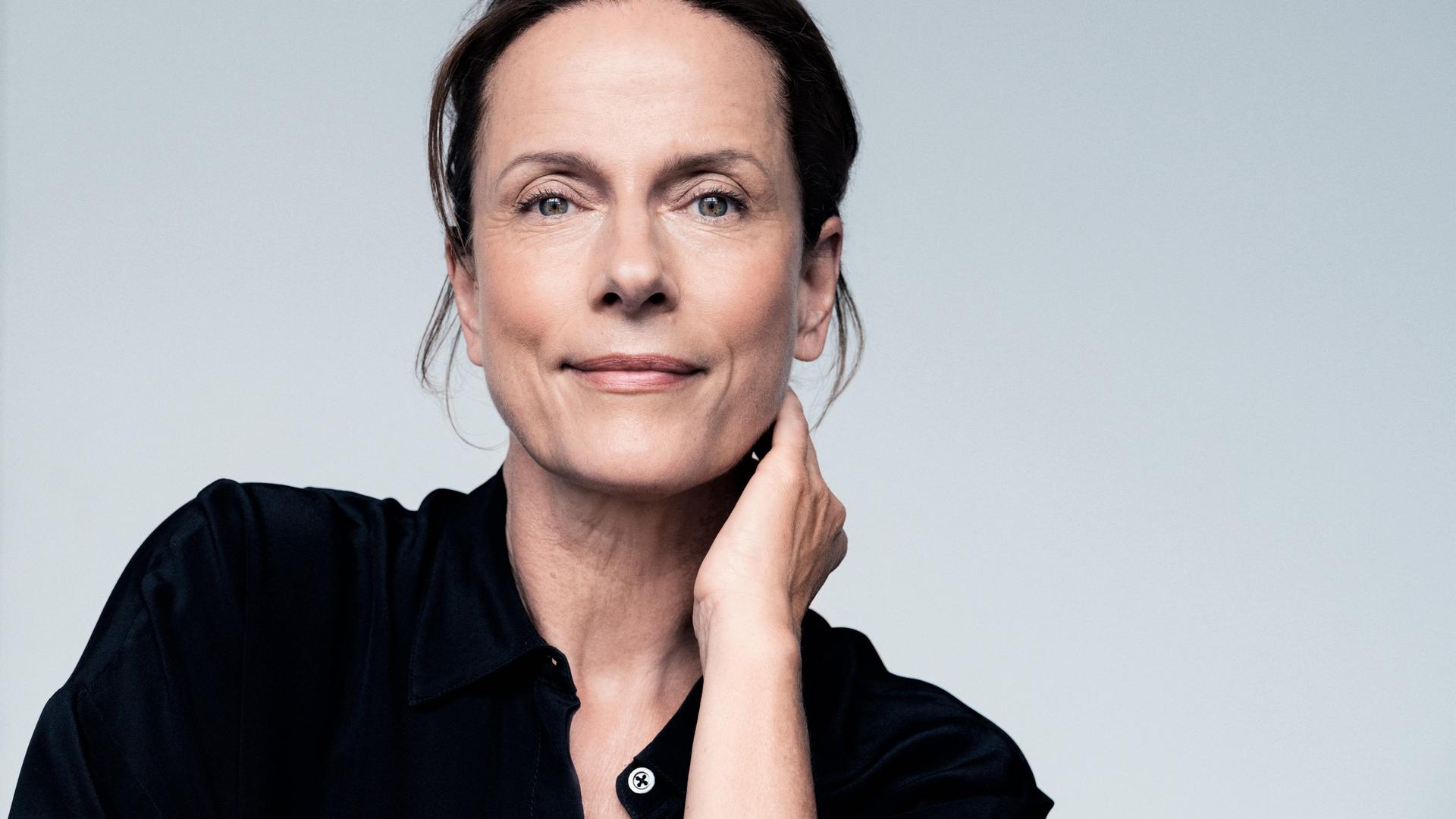 Claudia Michelsen lächelt in die Kamera. Sie trägt ein schwarzes Hemd und hat das Haar hochgesteckt.