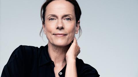 Claudia Michelsen lächelt in die Kamera. Sie trägt ein schwarzes Hemd und hat das Haar hochgesteckt.