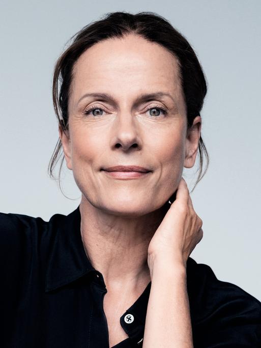 Claudia Michelsen lächelt in die Kamera. Sie trägt ein schwarzes Hemd und hat das Haar hochgesteckt.