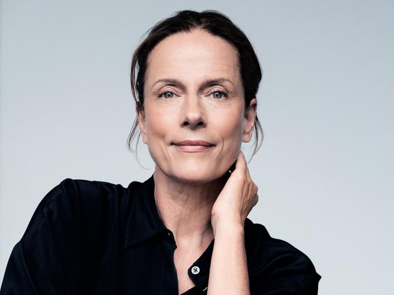 Claudia Michelsen lächelt in die Kamera. Sie trägt ein schwarzes Hemd und hat das Haar hochgesteckt.