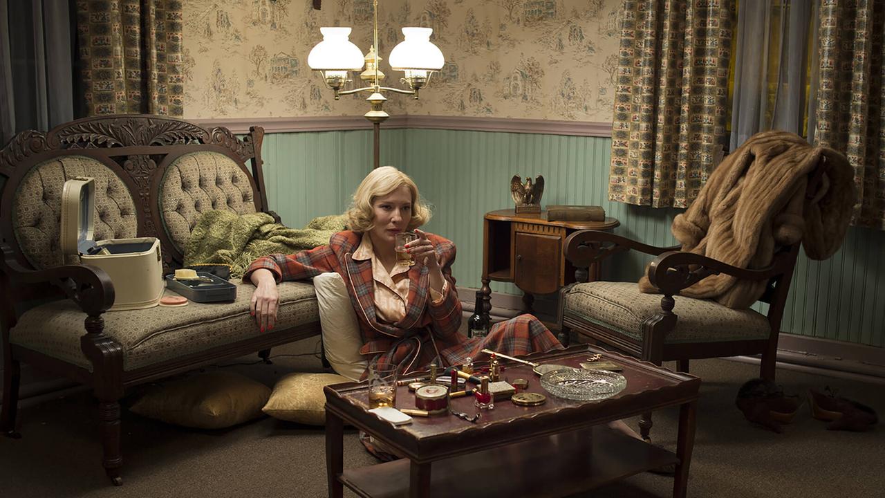 Cate Blanchett sitzt auf dem Boden eines Wohnzimmers im Stil der Fünfzigerjahre und trinkt Alkohol.